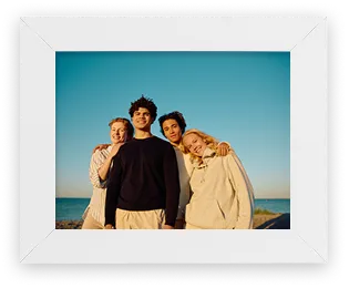 Framed photo of four friends smiling together on a beach at sunset, in a thin white frame.